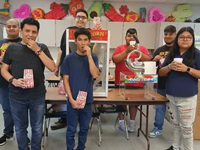 Group of students eating popcorn standing near popcorn machine