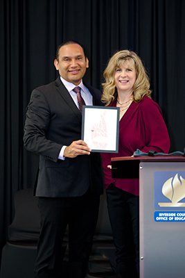 Dr. Edwin Gomez and April McArthur hold framed drawing of hand signing the letter R