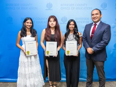 Three young women holding honors standing with Dr. Edwin Gomez
