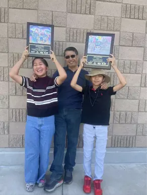 Gabby and Antonio each holding up an award with their father