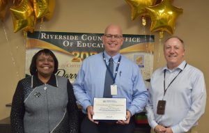 Man holding certificate of recognition standing with two dignitaries