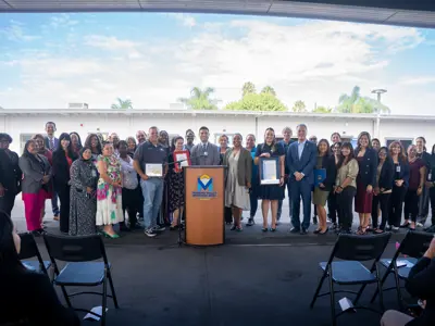 Group gathered around podium holding several framed honors