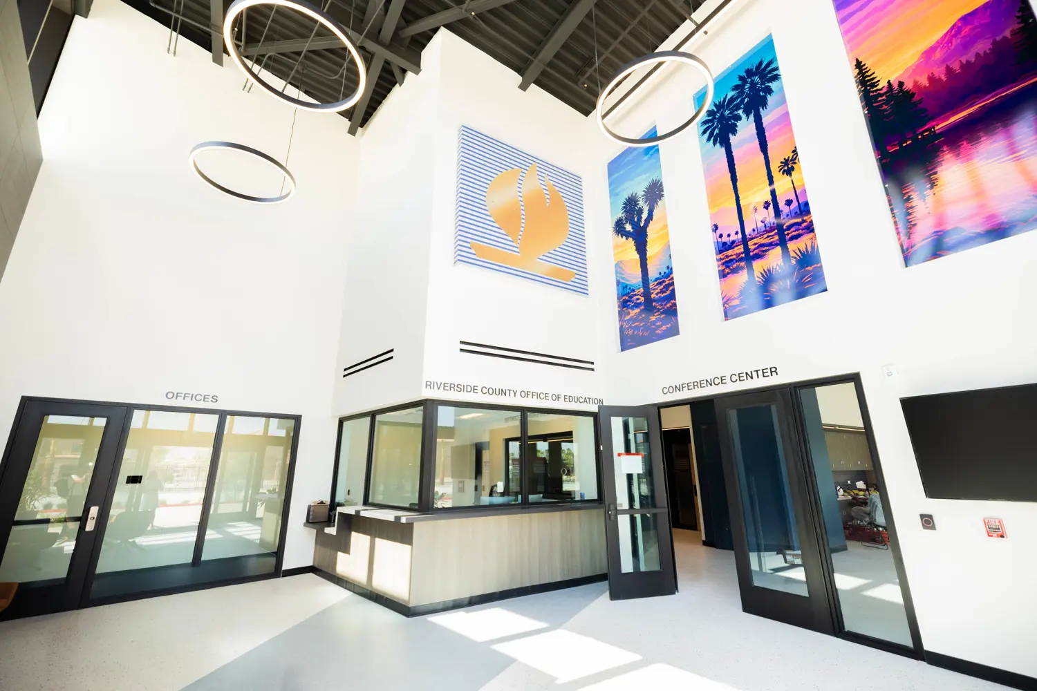 Bright lobby area with open ceiling construction and bright desert artwork alongside the Riverside County Office of Education logo. Doors lead to Offices and Conference Center
