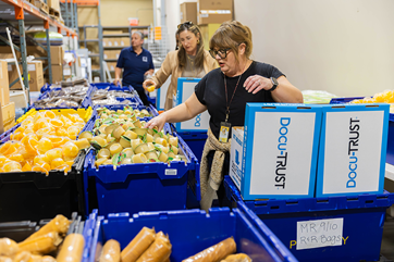 People packing boxes with groceries from large bins in warehouse