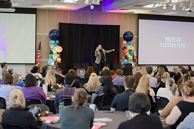 Wayne Betts on stage with slide that reads Write Me a Lesson Plan