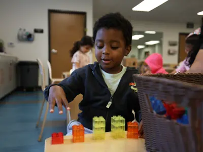 Young boy counting showing three fingers to show count of blocks